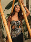 Woman wearing a leopard print top with a scarf, standing among bamboo and tropical plants.